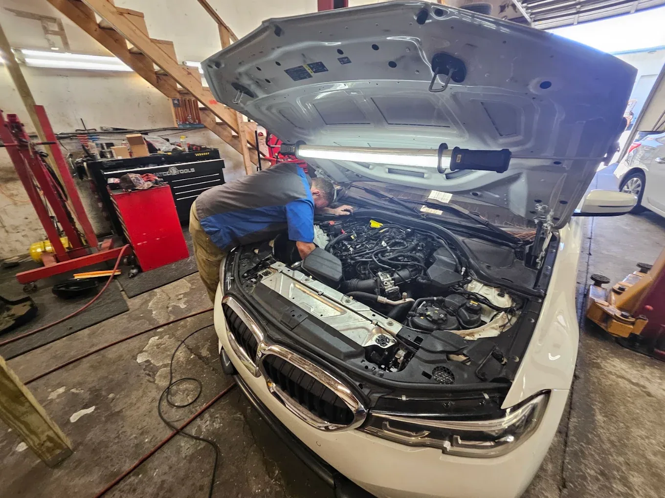 A technician working under the hood of a white BMW