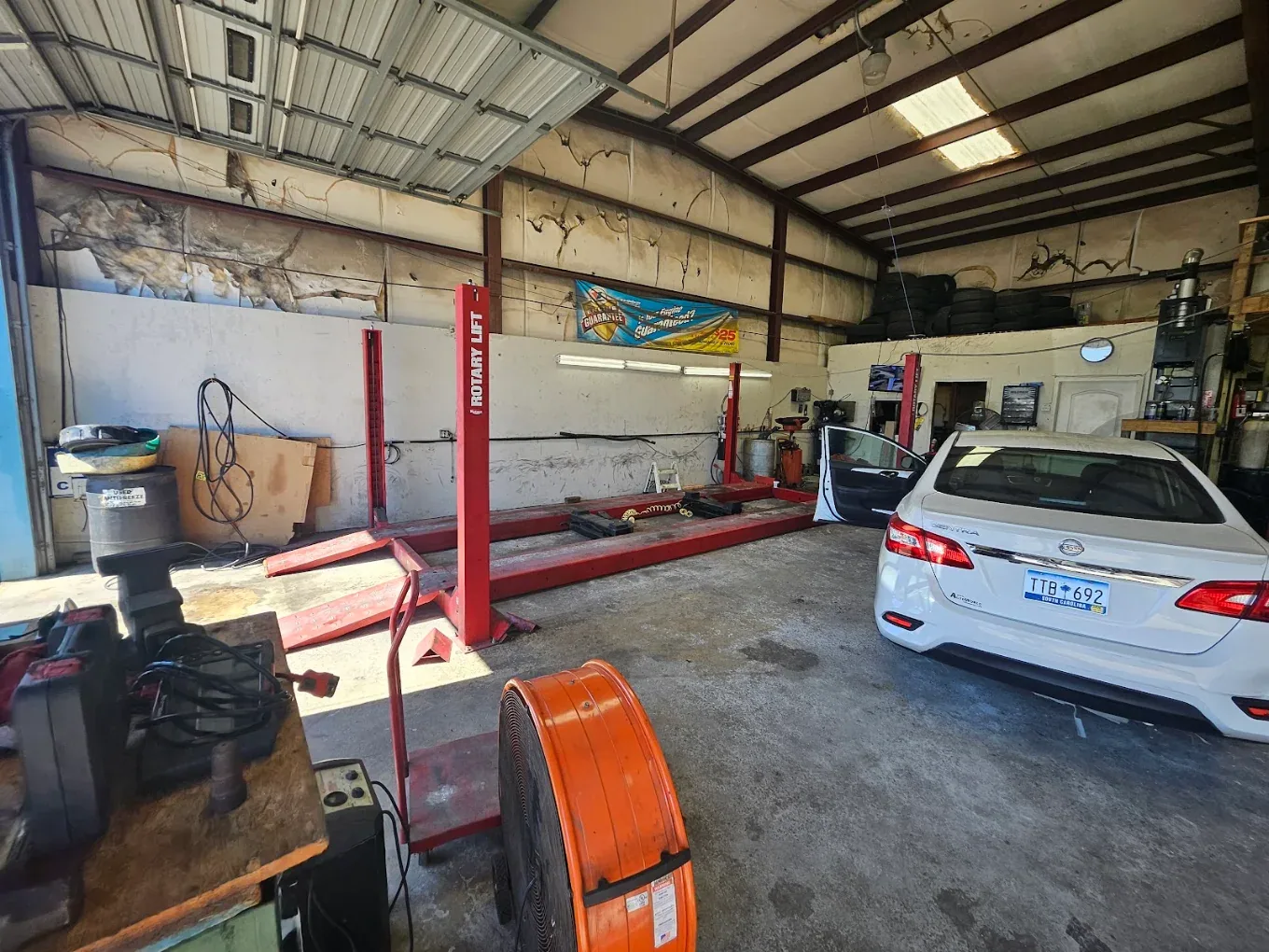 A white sedan on a red lift in an open bay